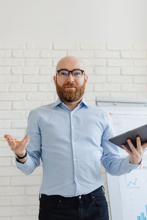 Free Bald man with beard presenting with a tablet in a modern office setting. Stock Photo