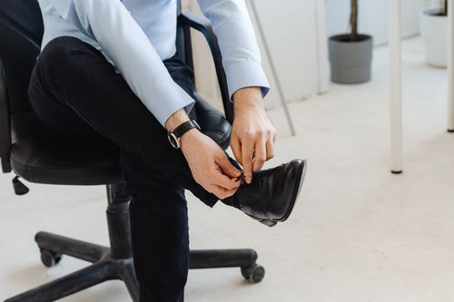 Free Person in smart casual attire, indoors, tying shoelaces, creating a business-ready look. Stock Photo