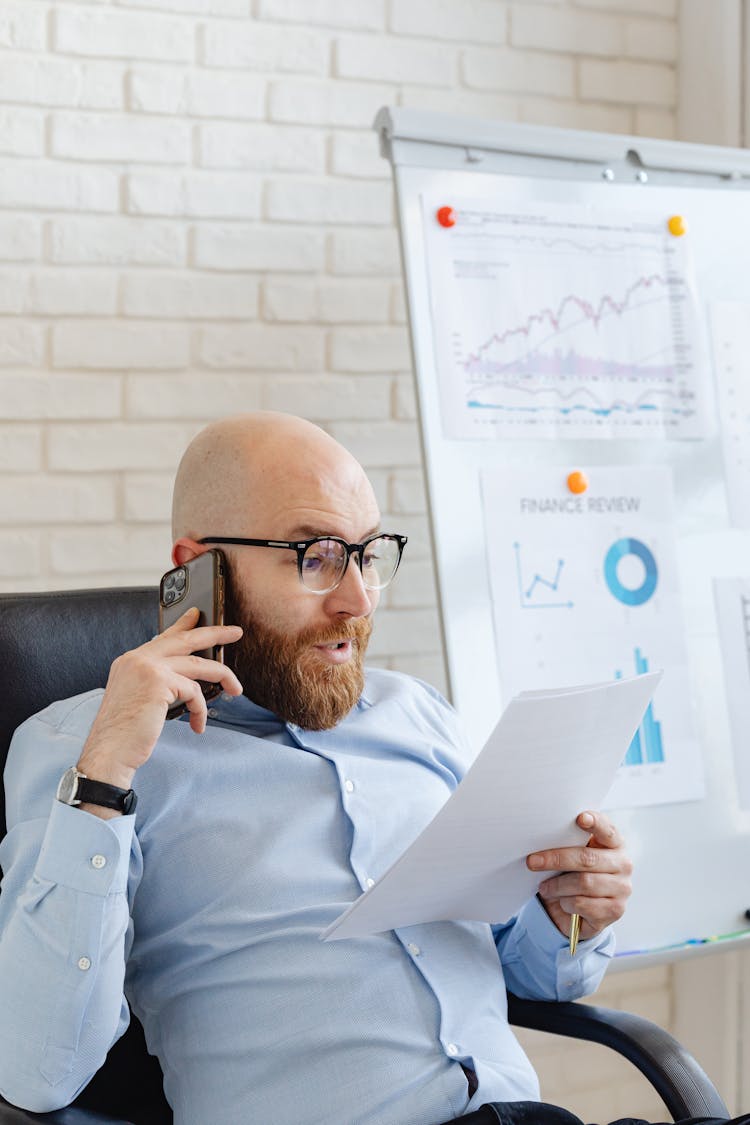 A Man Talking On The Phone While Looking At Documents