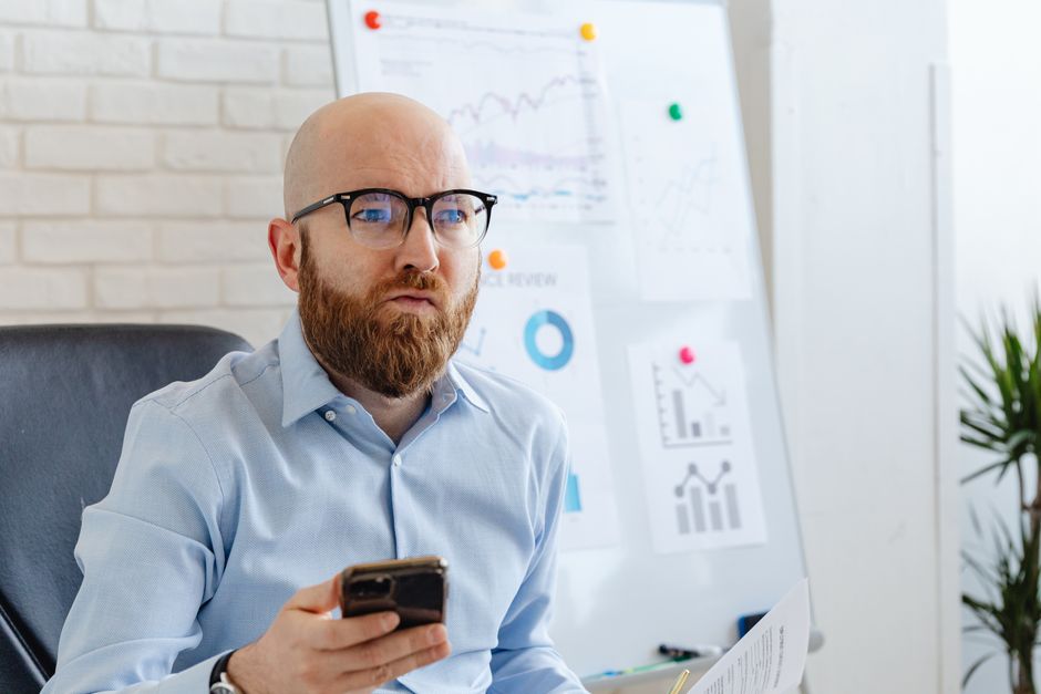 Bald man with beard holding smartphone in office setting, focused on business presentation. Bald man with beard holding smartphone in office setting, focused on business presentation.