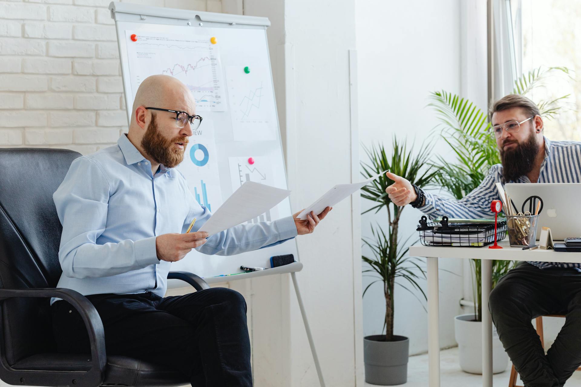 Two men engaging in a business meeting, analyzing graphs and documents in an office.