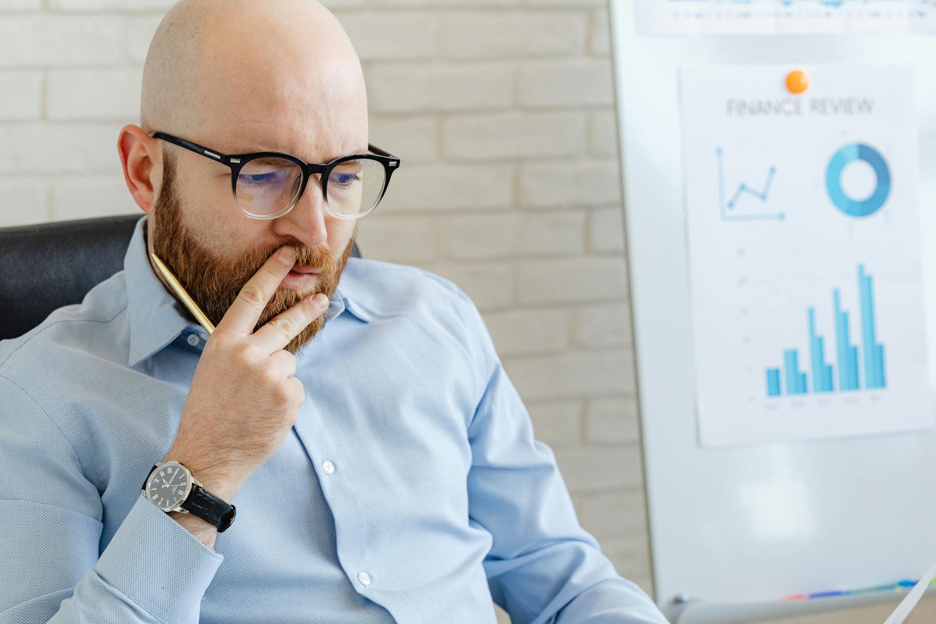 Business analyst in a blue shirt analyzing financial charts on a whiteboard.