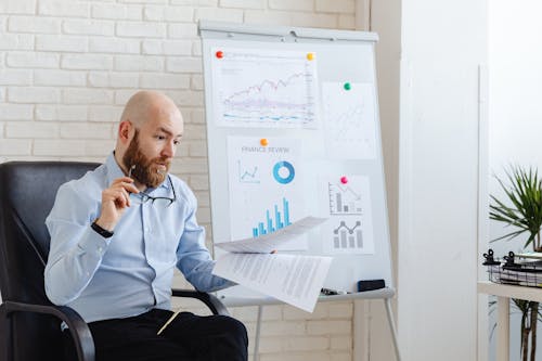 Man in Blue Long Sleeves Sitting Near the White Board 