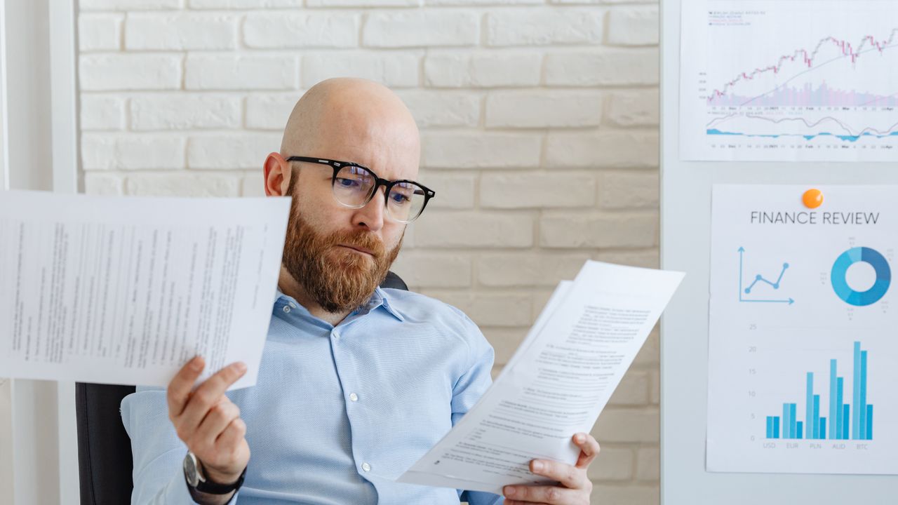 Bald bearded businessman reading financial documents in modern office setting.