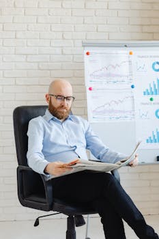 Caucasian man in corporate attire reading newspaper by business charts indoors.