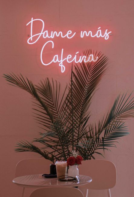 Trendy coffee shop setup featuring palm decor, neon sign, and cozy seating.