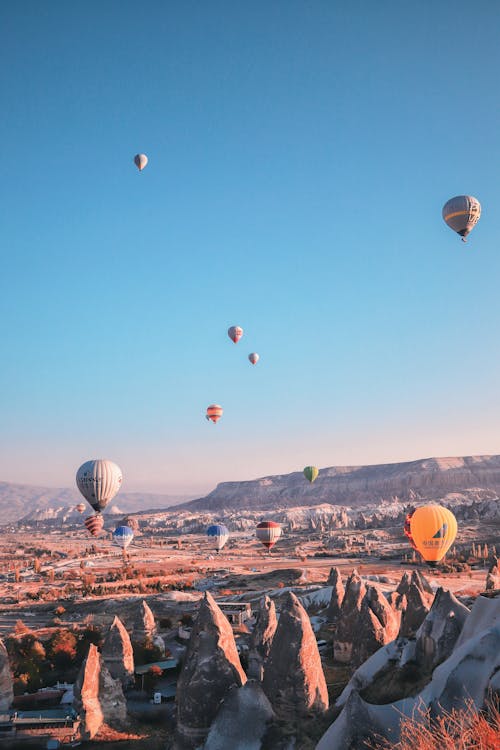 Many colorful hot air balloons flying in cloudless blue sky over mountains in Cappadocia in Turkey