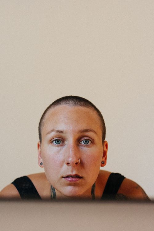 Free Close-up headshot of a woman with short hair and a nose piercing, neutral background. Stock Photo