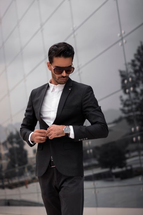 Free A fashionable man in a black suit adjusting his jacket outdoors in Dubai. Stock Photo