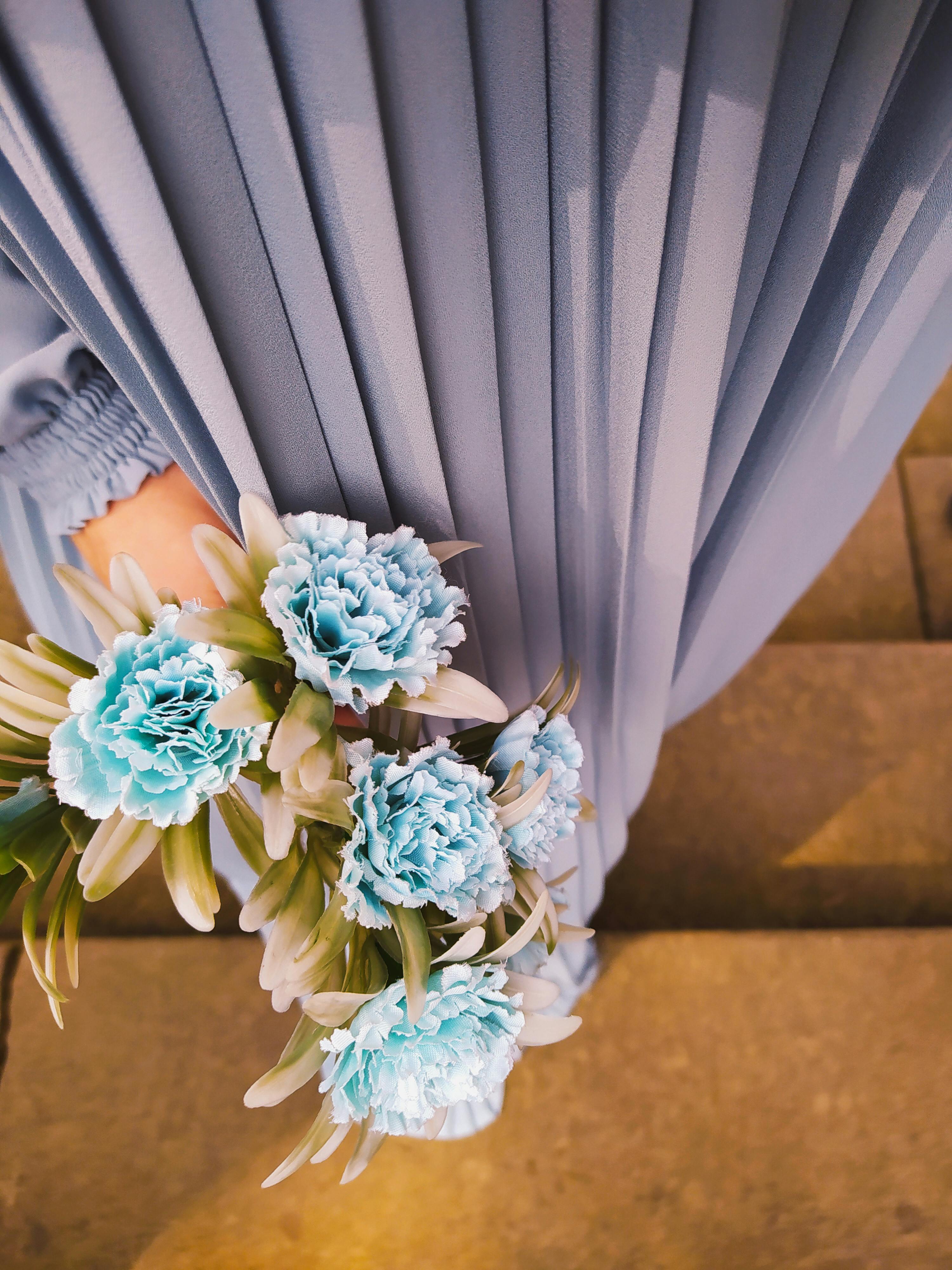 A closeup of a hand holding blue carnations against a pleated dress background.