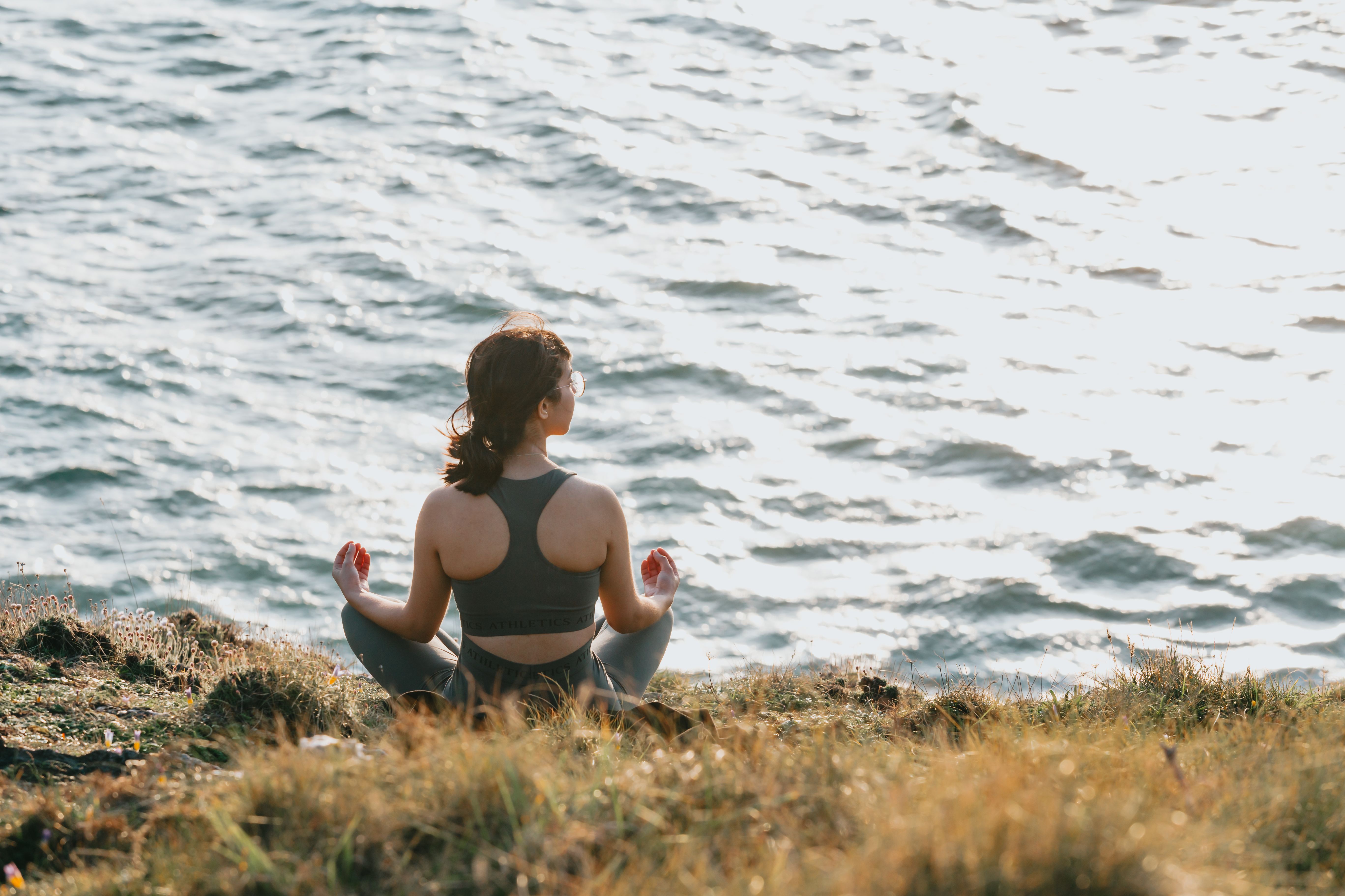 Woman practicing meditation overlooking the ocean at sunset