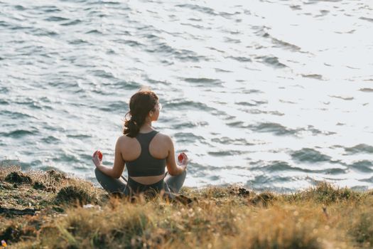 A woman practices meditation overlooking the ocean at sunset, achieving relaxation and peace.