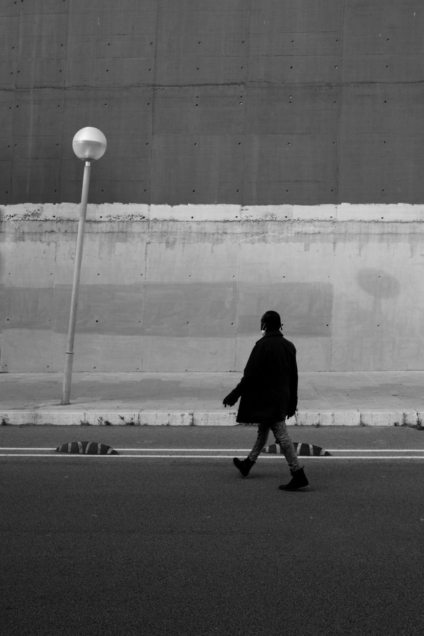 Black and white photo of a person walking past an urban wall, capturing a minimalist street scene.