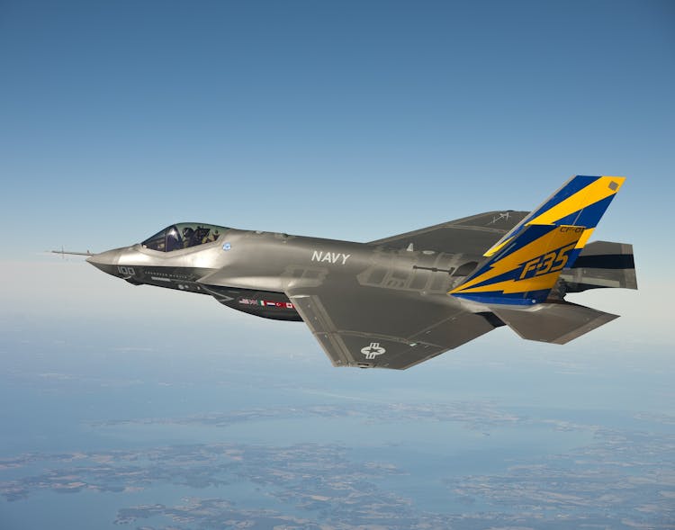 Grey Blue And Yellow Navy F 35 Fighter Plane Flying On Clear Blue Sky