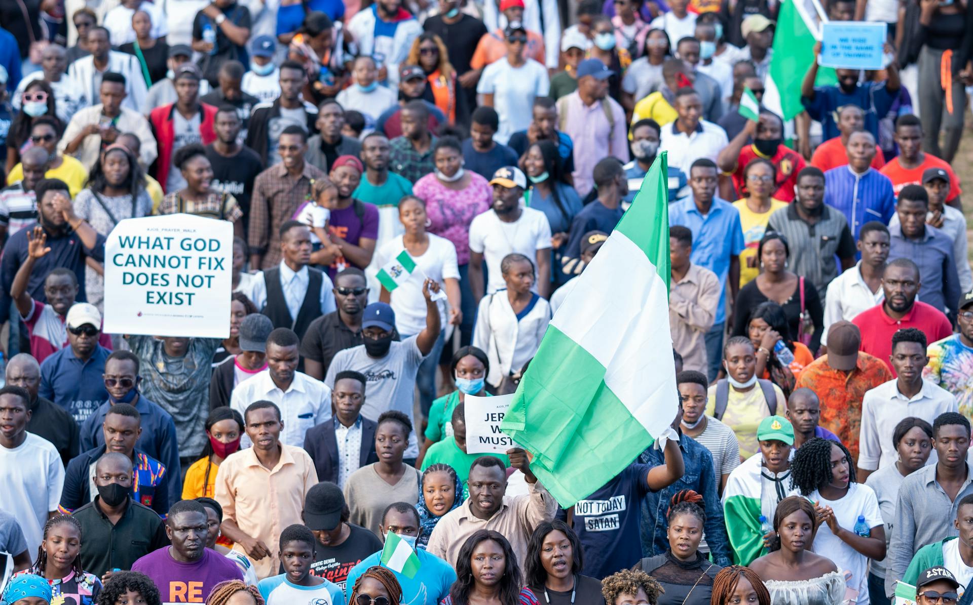 Diverse group gathered for a protest holding Nigerian flags and signs.