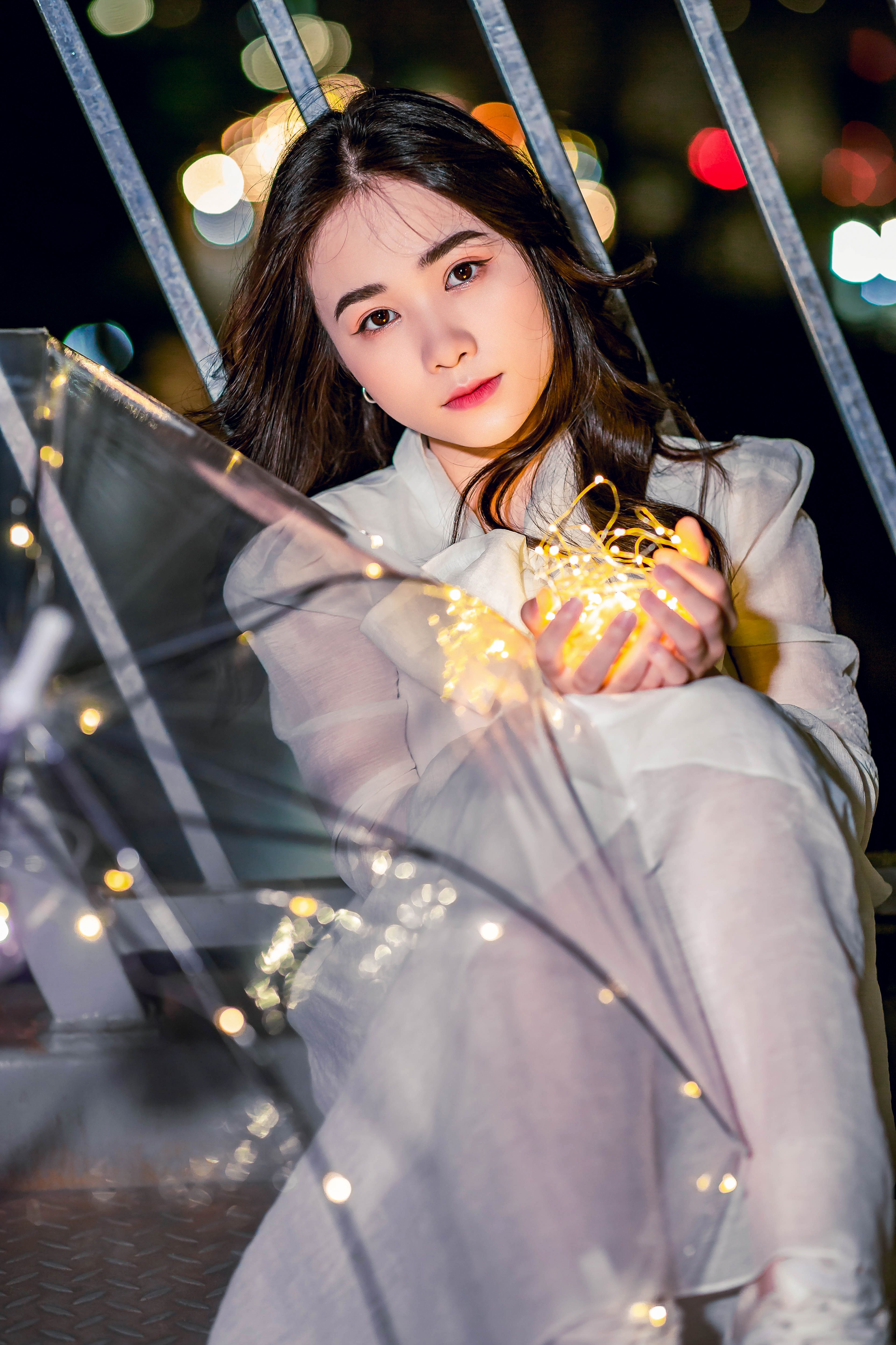 Close-up of an Asian woman posing with string lights at night, exuding a warm and vibrant mood.