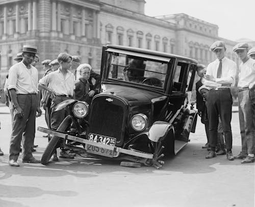 Grayscale Photo of People Standing near the Wrecked Vintage Car