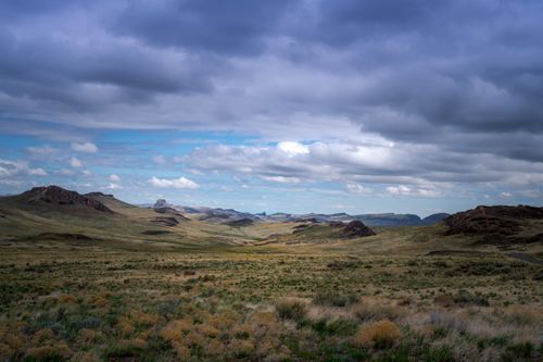 Free Picturesque landscape of grassy field and hills located in countryside under cloudy sky in daytime Stock Photo