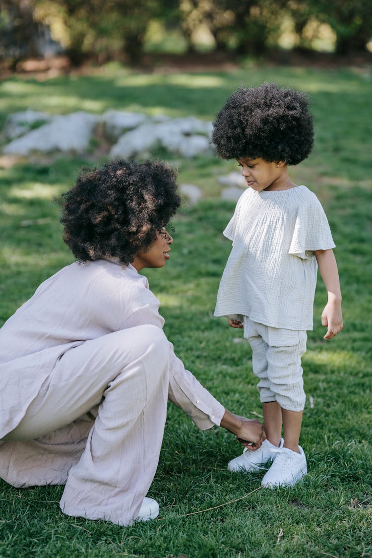 Curly Haired Woman Tying The Girl's White Shoes 