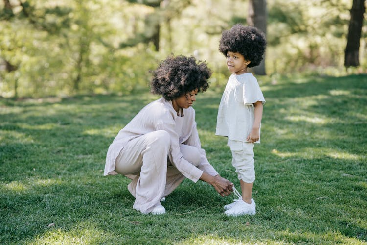 Curly Haired Woman In Long Sleeve Shirt Tying The Kid's Shoes 