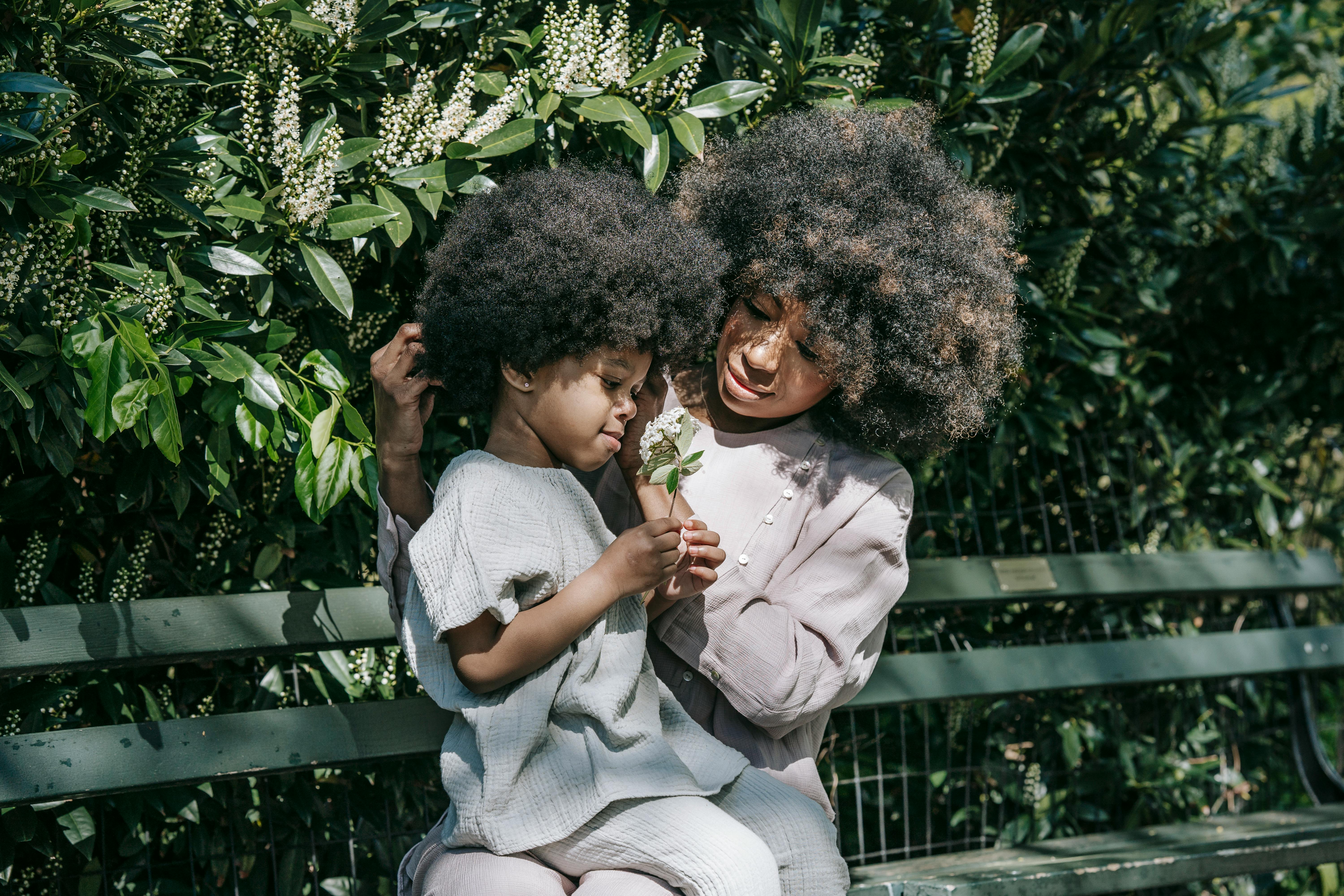 African American mother and child bonding outdoors on a park bench surrounded by greenery.