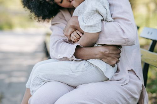 Free A mother lovingly embraces her child on a wooden bench in a serene outdoor setting. Stock Photo