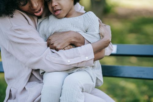 Free A tender moment between a mother and her child, sitting and hugging on a bench outdoors. Stock Photo