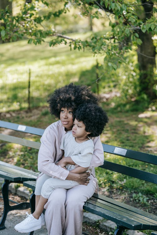 Free A Woman Hugging her Daughter while Sitting on a Wooden Bench Stock Photo