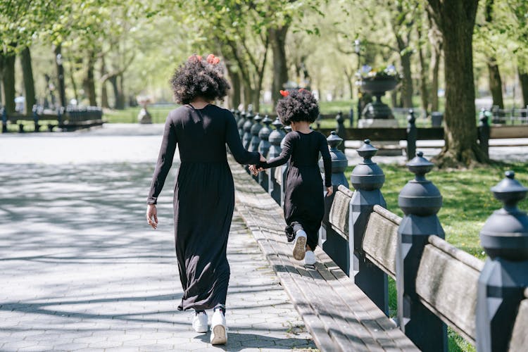 Back View Of A Mom And Daughter Holding Hands While Walking At A Park