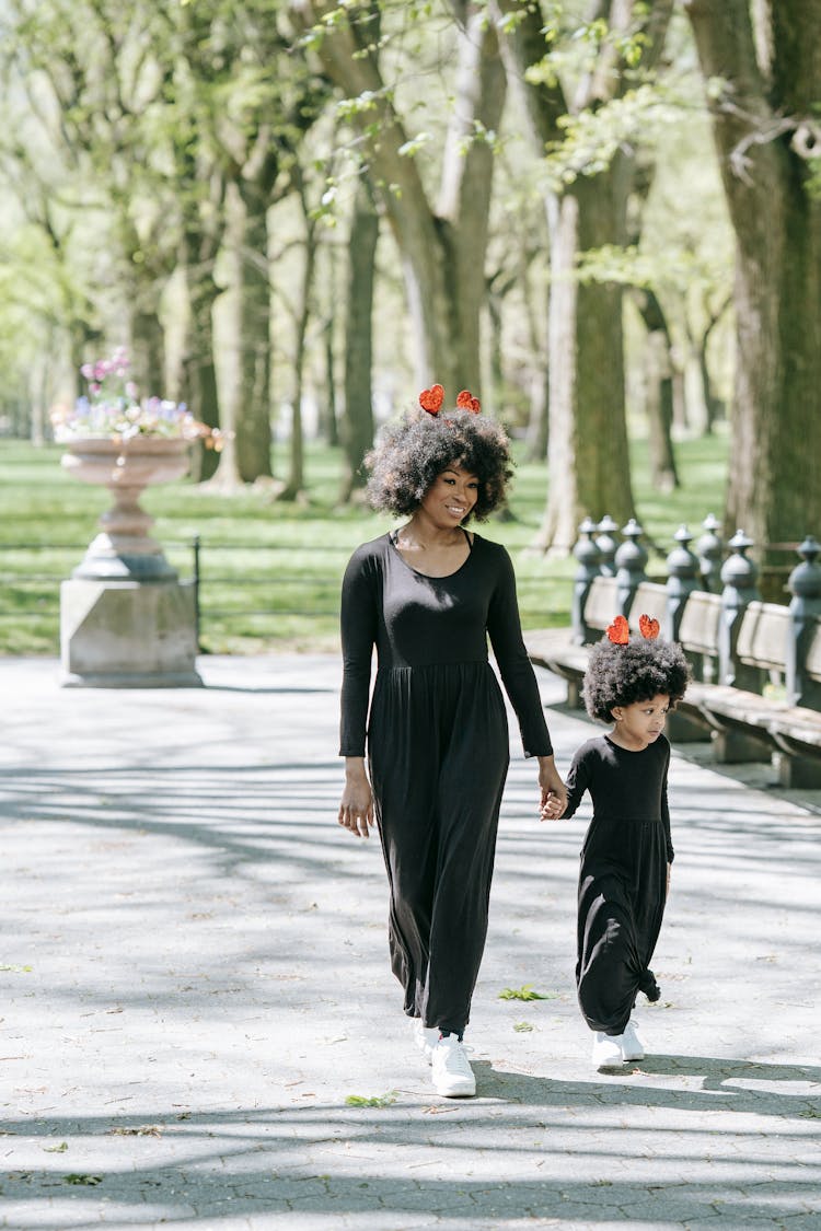 A Woman And A Girl In Matching Outfits Walking In The Park