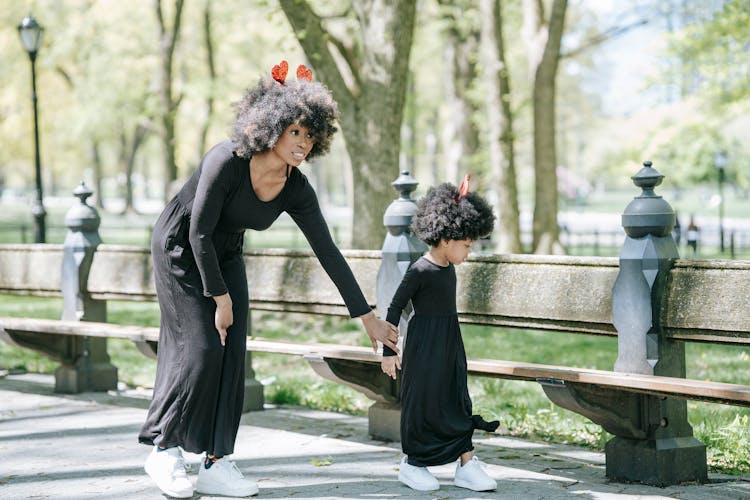 A Woman And Her Daughter Holding Hands While Walking At A Park