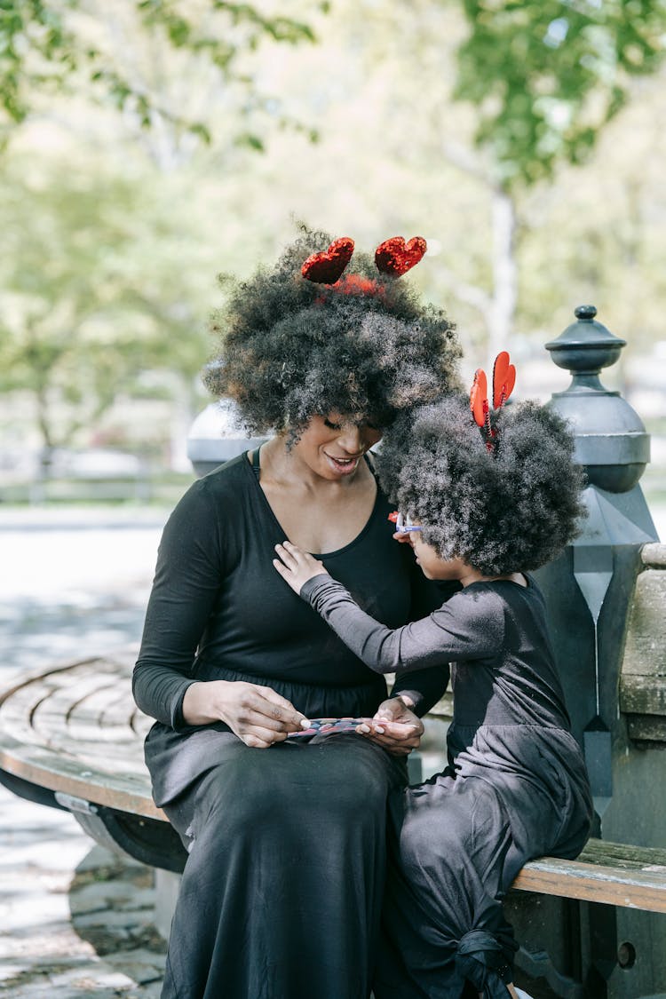 A Woman And A Girl Sitting On A Park Bench Wearing Matching Costumes