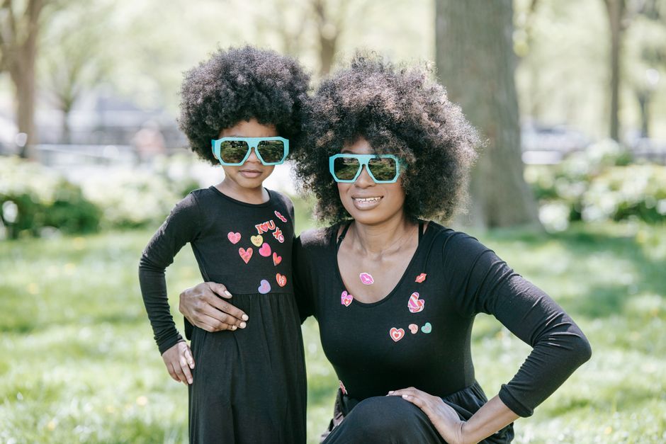 Mother and daughter wearing matching dresses and sunglasses, enjoying a sunny day in the park.