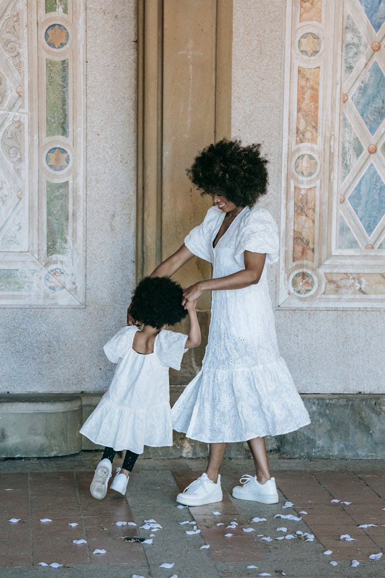 A Woman And A Girl In White Dresses Dancing On A Floor With Flower Petals