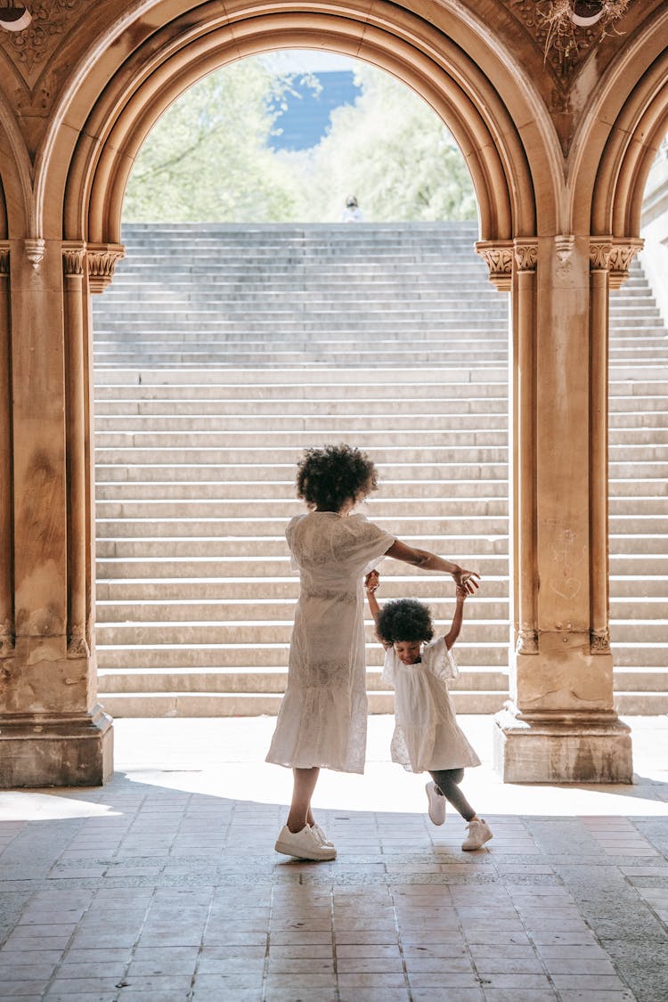 A Woman Dancing With Her Daughter By An Arch