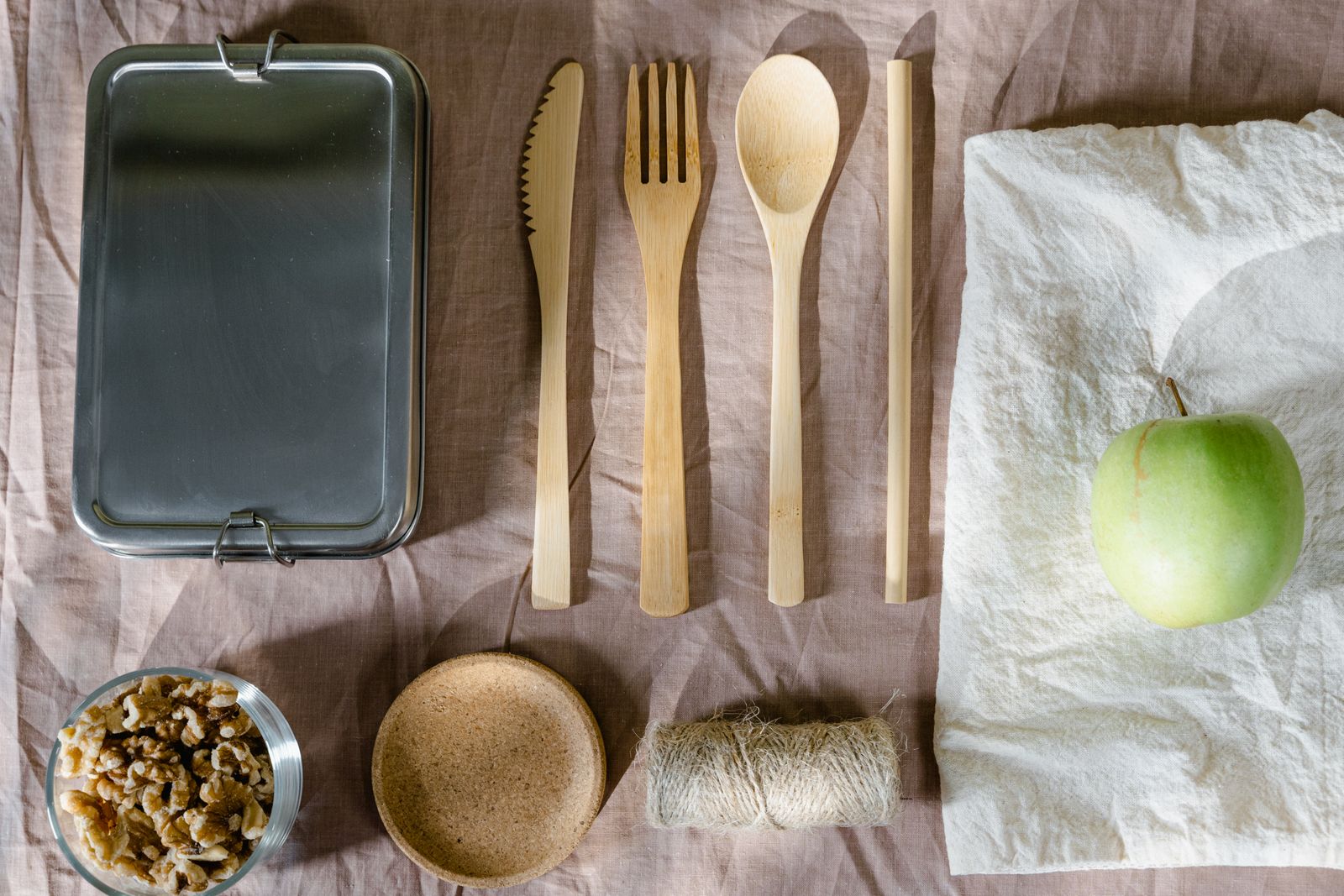 Sustainable flat lay arrangement with wooden utensils, green apple, and lunch box.