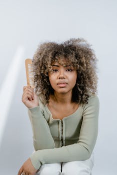 Portrait of a woman with natural afro hair holding a wooden comb, emphasizing beauty routines.