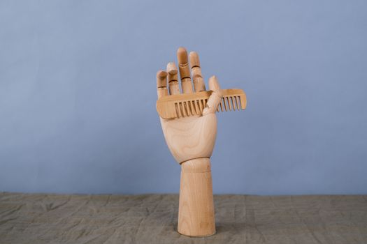 Artistic wooden hand sculpture holding a comb on a neutral backdrop. Minimalist and creative display.