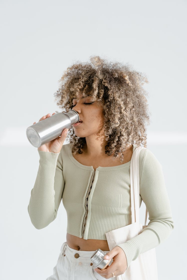 A Woman Drinking From A Stainless Jug