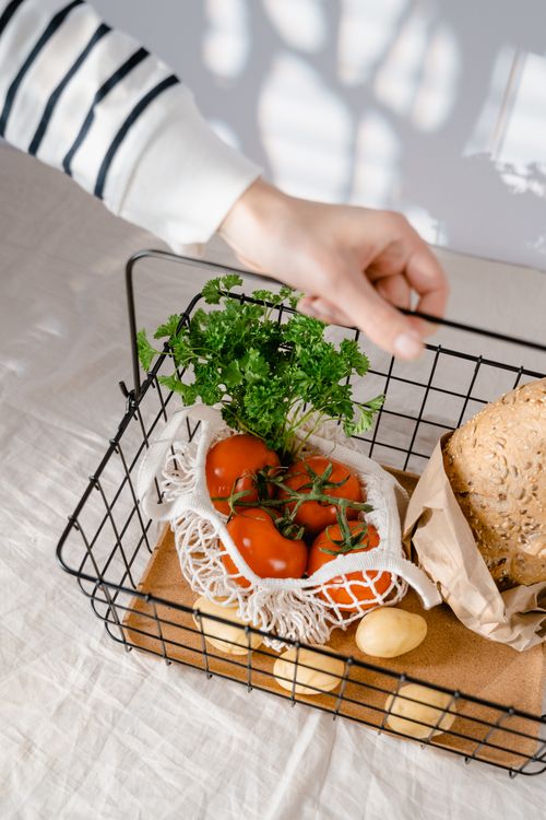 Free Hand reaching for fresh tomatoes in an eco-friendly vegetable basket with bread. Stock Photo