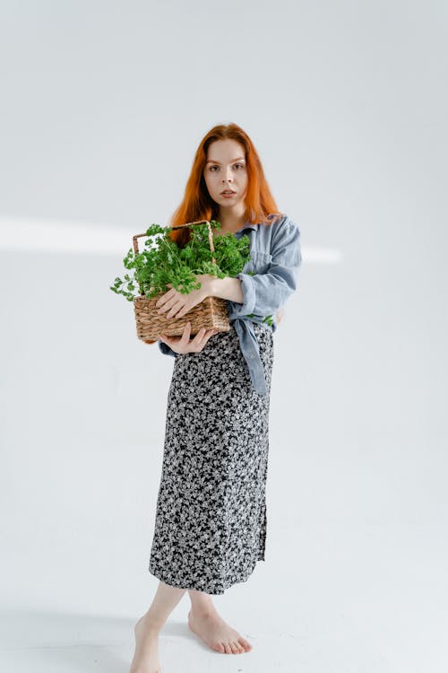 A Woman in Black and White Dress Holding a Basket of Green Leaves