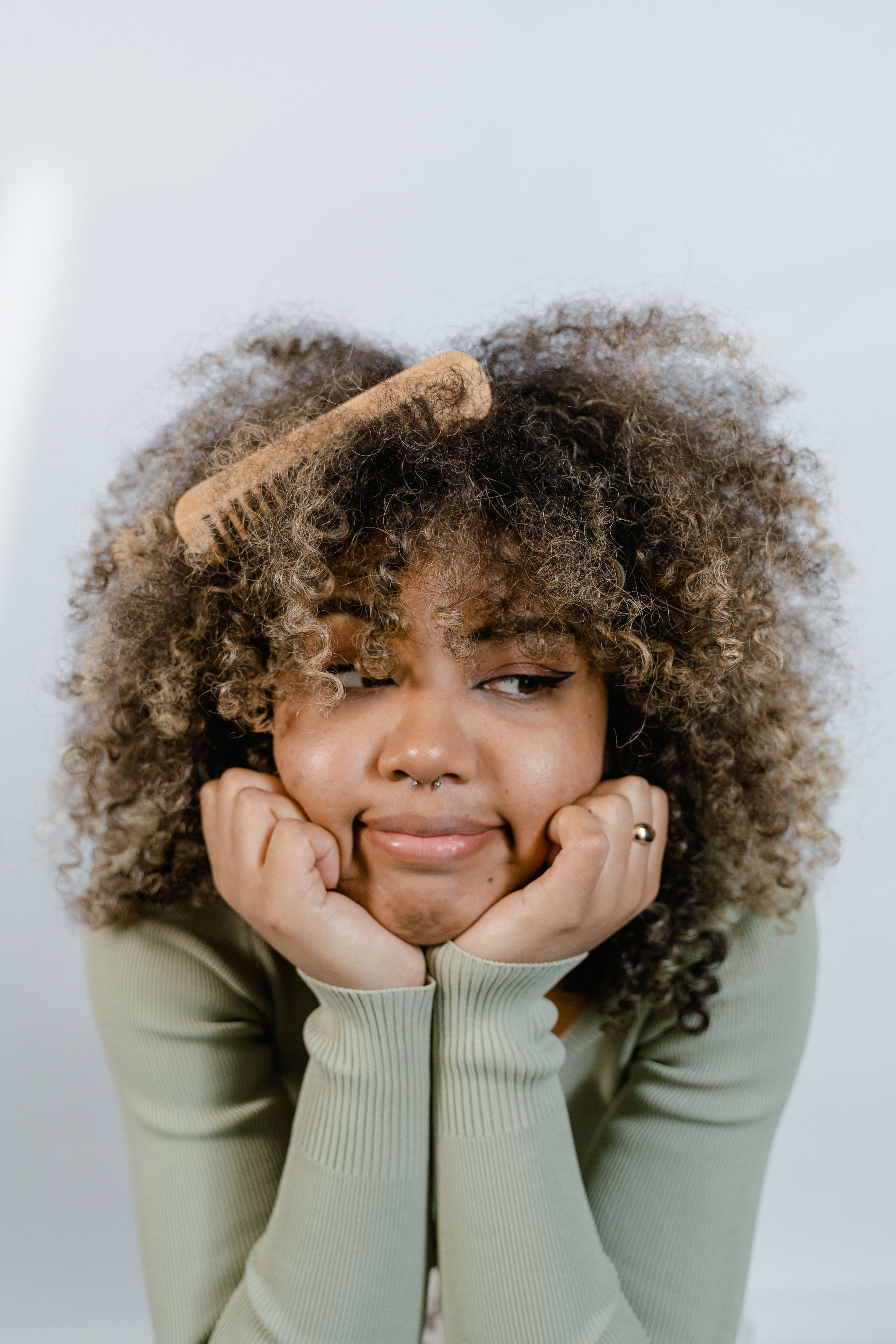 Free Thoughtful woman with curly hair posing with hands under chin and wooden comb. Stock Photo