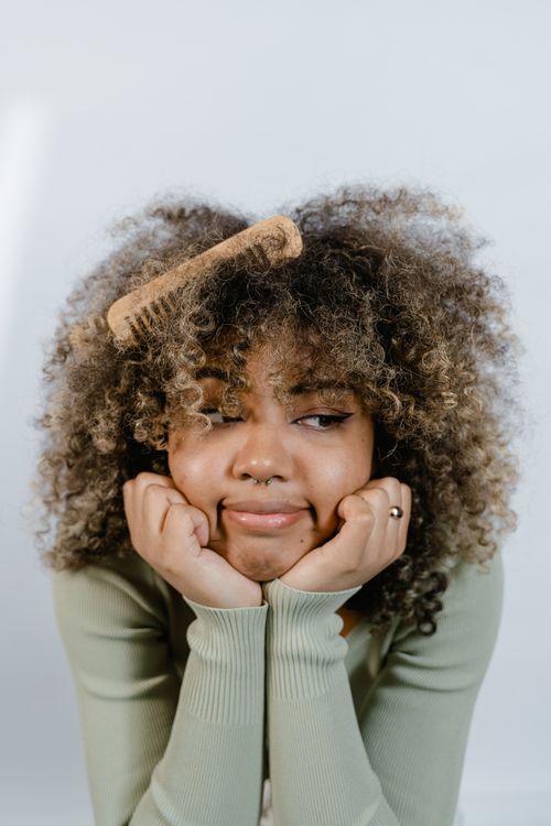 Free Thoughtful woman with curly hair posing with hands under chin and wooden comb. Stock Photo