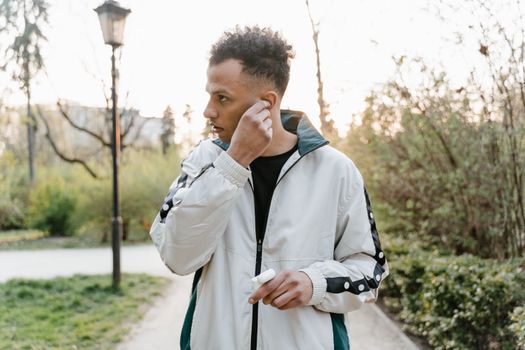 A young man in a park adjusts his wireless earbuds during a jogging session, with a serene outdoor background.