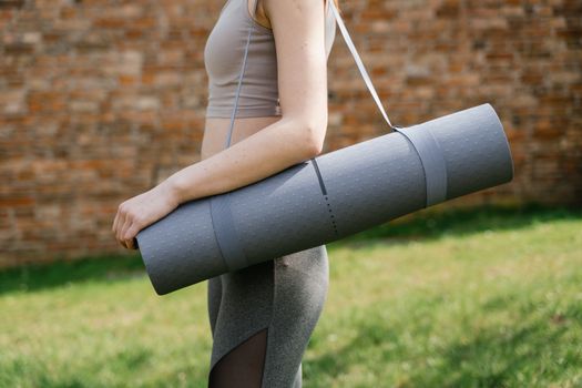 Woman holding a yoga mat outdoors, ready for exercise in the sun.