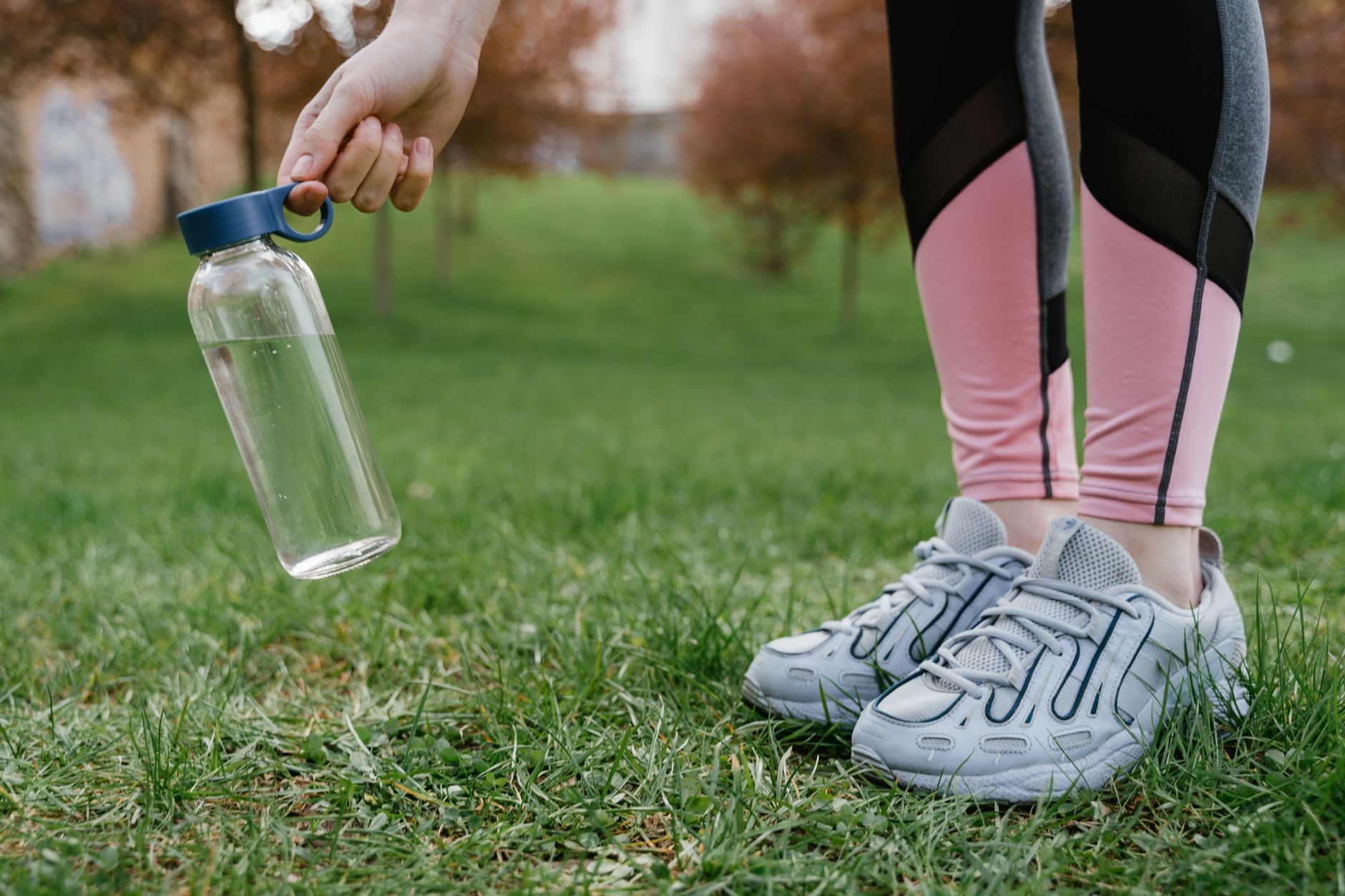 diosmin hesperidin for varicose veins — Close-up of legs in pink leggings and sneakers with a glass water bottle in hand on grass.
