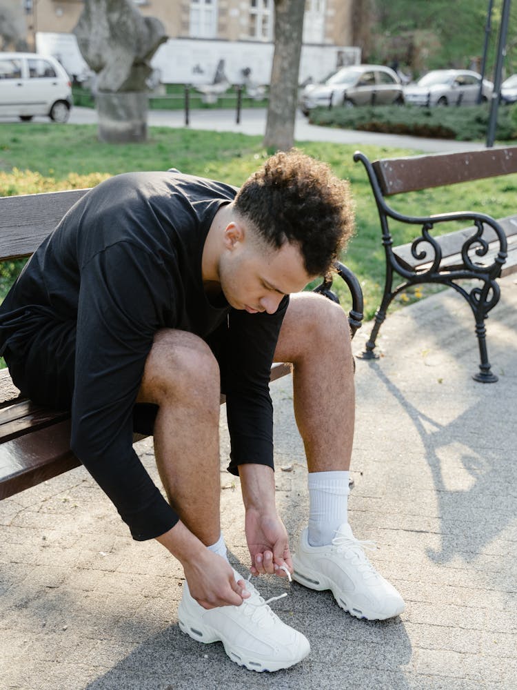 A Man Sitting On A Wooden Bench Tying His Shoe Lace