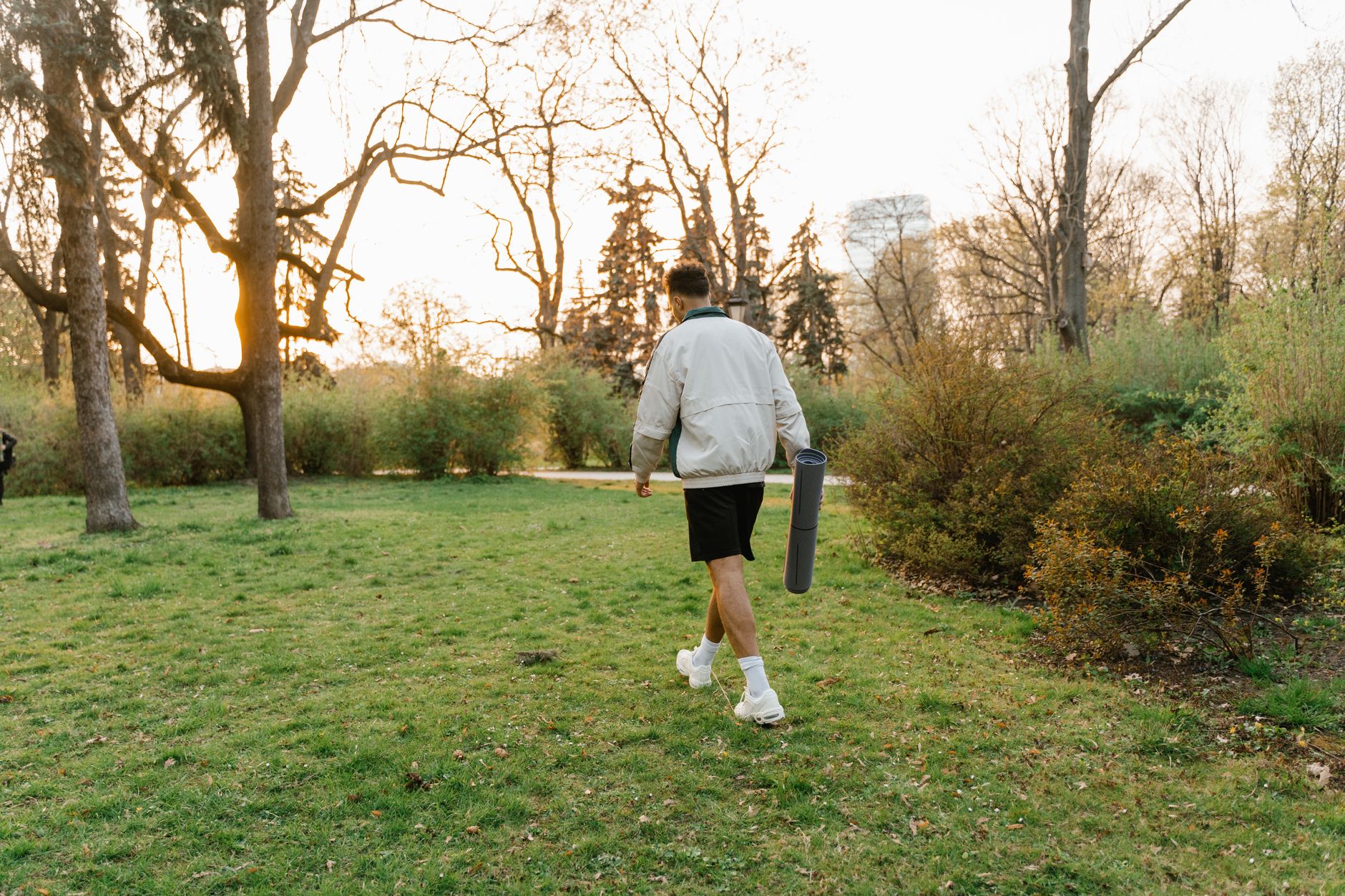 A person strolls through a park with a yoga mat, capturing the tranquil essence of nature at sunset.