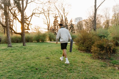 Free A person strolls through a park with a yoga mat, capturing the tranquil essence of nature at sunset. Stock Photo