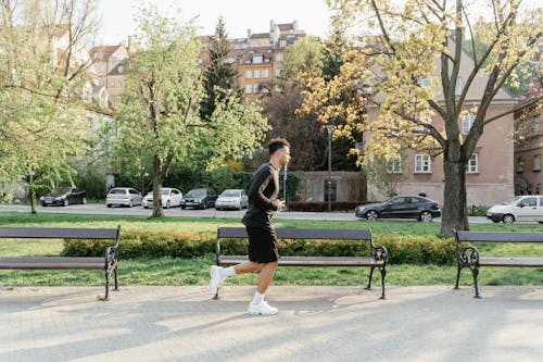 A Man in Active Wear Running Near Park Benches